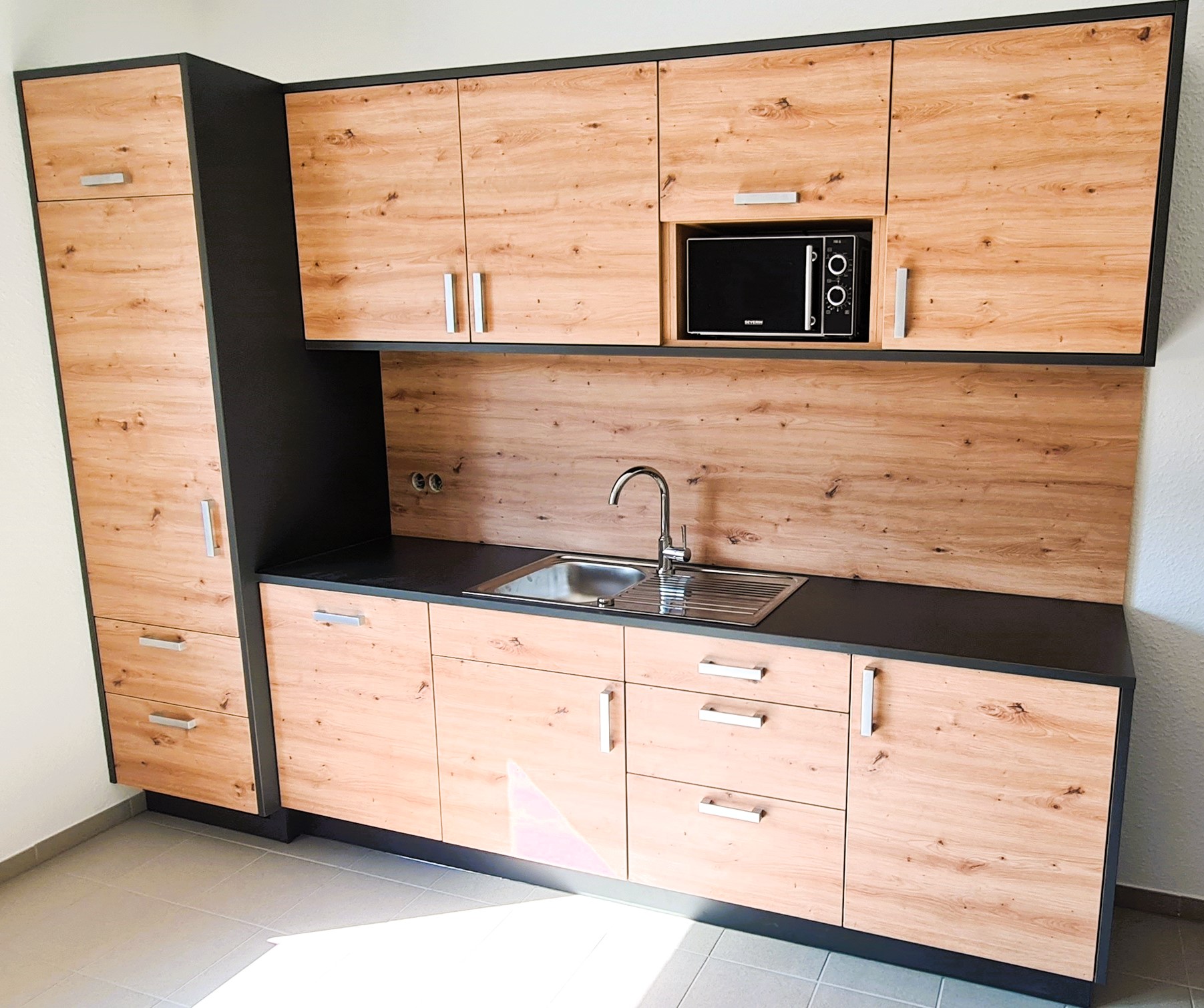 Schreinerküche in Holzoptik mit dunklen Akzenten, wie Arbeitsplatte und Korpi