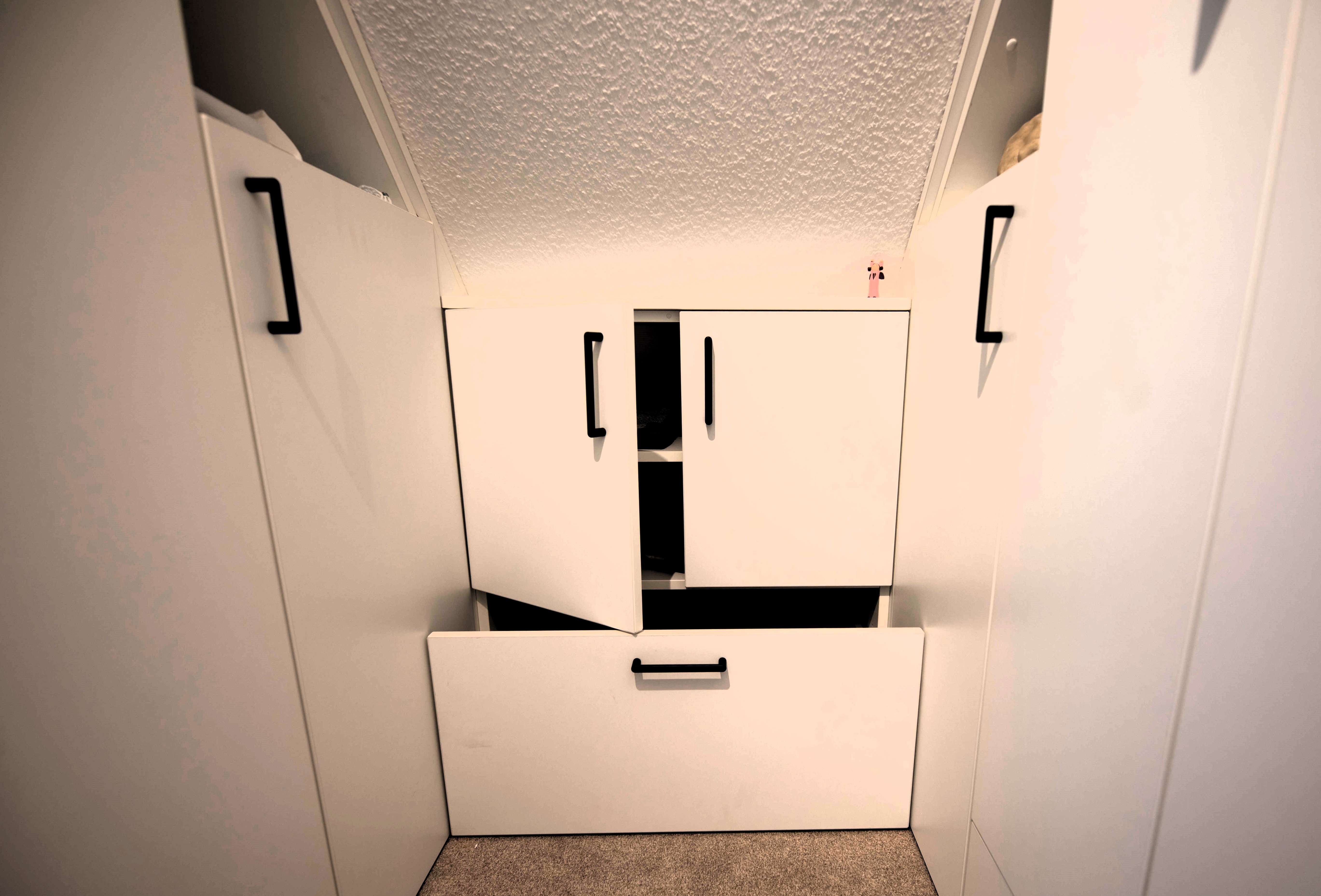 weiße Schränke mit schwarzen Griffen eingepasst unter einer Dachschräge