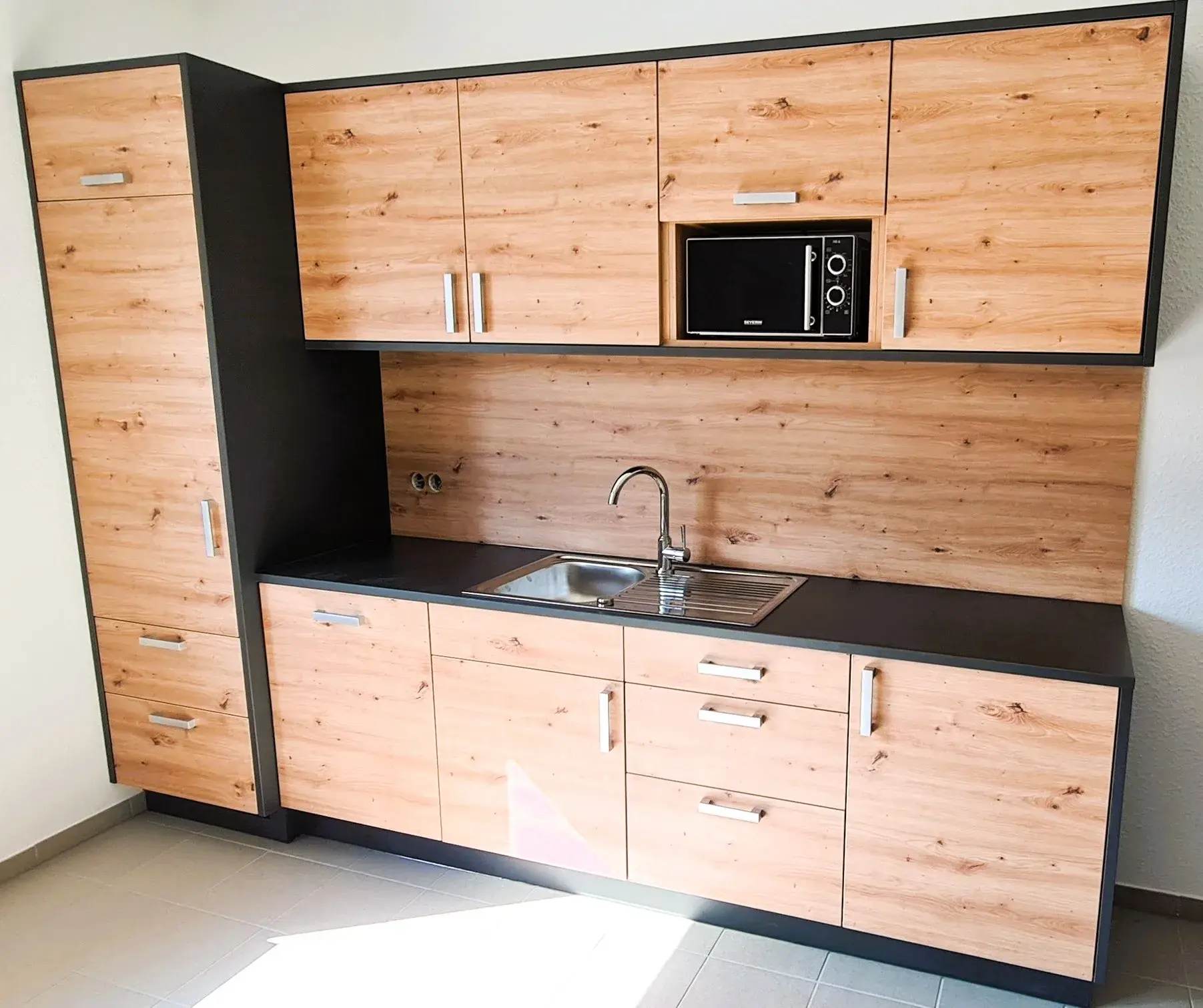 Schreinerküche in Holzoptik mit dunklen Akzenten, wie Arbeitsplatte und Korpi