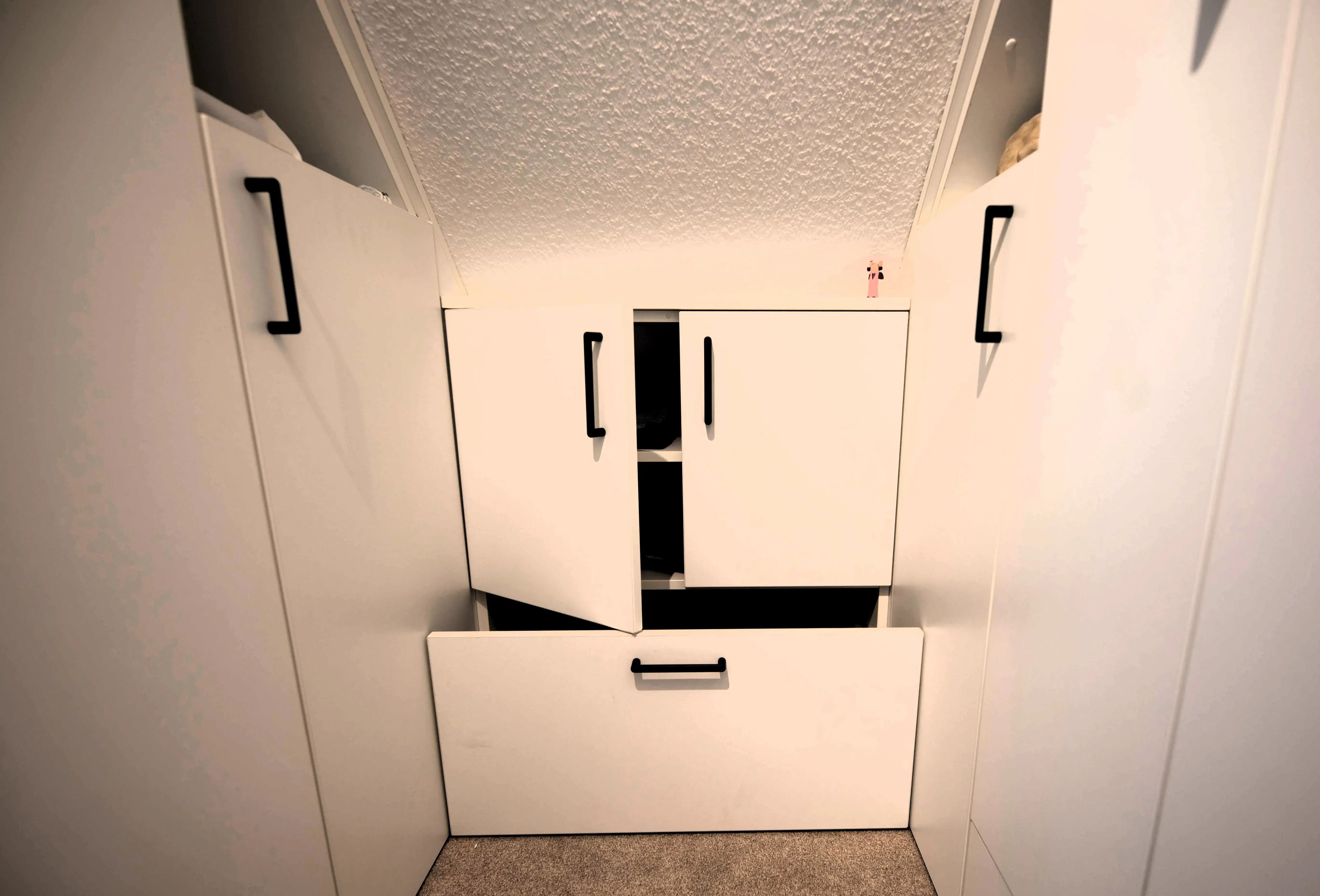 weiße Schränke mit schwarzen Griffen eingepasst unter einer Dachschräge
